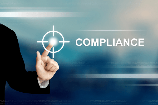 COMPLIANCEの文字とターゲットマークに指を合わせているビジネスパーソンの手元。